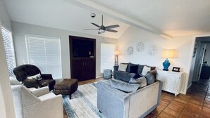 Un salon comprenant un canapé, des fauteuils, une table basse, un téléviseur et un ventilateur de plafond.