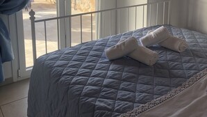 Ein Schlafzimmer mit einem Bett, einem Kleiderschrank und Blick auf ein Steinhaus durch ein Fenster.