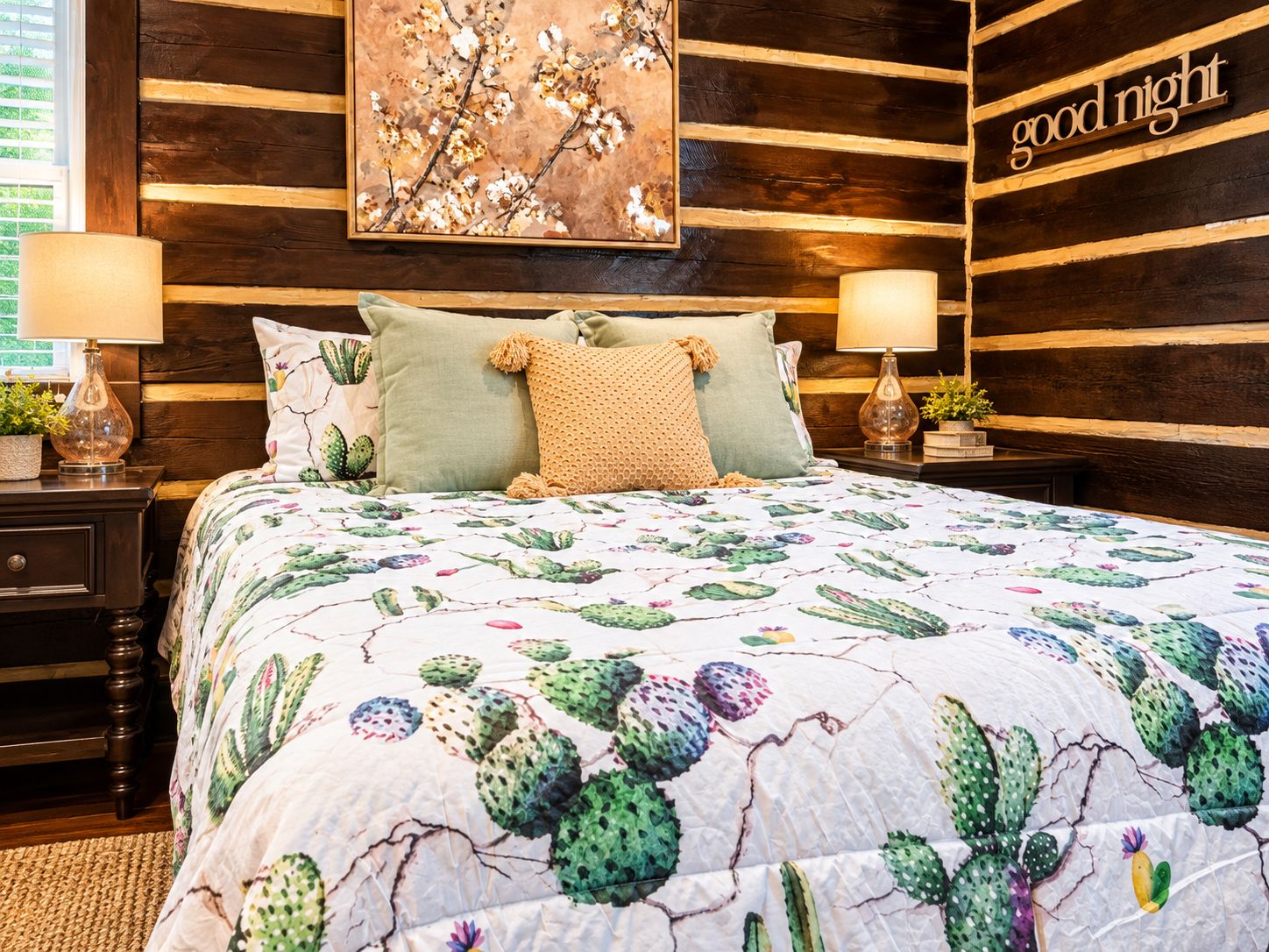 A bedroom with a cactus-themed bedspread, two bedside lamps, a nightstand with a plant, and a wall-mounted sign that reads 'good night'.