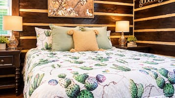 A bedroom with a cactus-themed bedspread, two bedside lamps, a nightstand with a plant, and a wall-mounted sign that reads 'good night'.