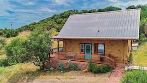 Ein einstöckiges Steinhaus mit Metalldach, einem umzäunten Veranda und einem kleinen Garten.