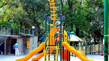 A playground with a yellow slide, a climbing structure, and a covered seating area.