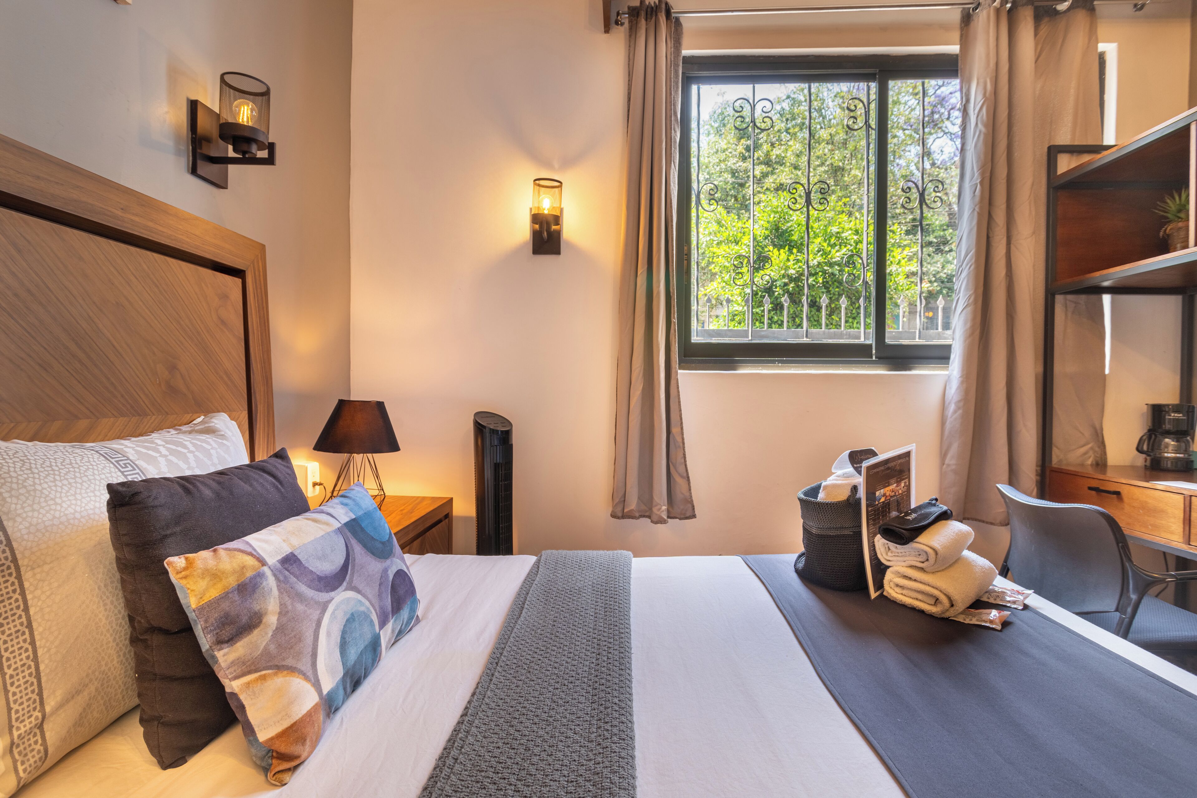 A hotel room with a large bed, a desk, a chair, a window with curtains, and a lamp.