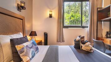 A hotel room with a large bed, a desk, a chair, a window with curtains, and a lamp.