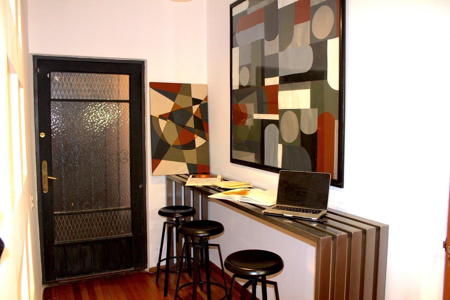 A modern interior with a black door, a laptop on a counter, and abstract art on the wall.