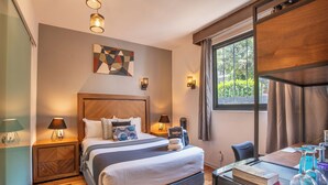 Een hotelkamer met een groot bed, twee nachtkastjes met lampen, een bureau met stoel, een raam met gordijnen en een geometrisch kunstwerk aan de muur.