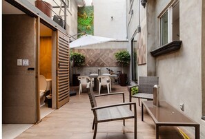 A narrow outdoor patio with a dining table and chairs, a bench, and a small table with a chair.