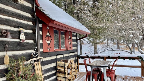 Una baita di legno con un patio in legno, un tavolo con sedie rosse e un camino.