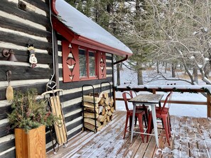 Una cabaña de troncos con una terraza de madera, una mesa y sillas rojas, y una chimenea.