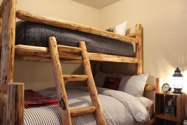 Una cama litera con escalera de madera, ropa de cama a rayas y una mesita de noche con un reloj y un farol.