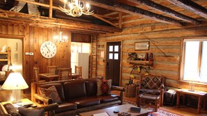 L'interno rustico di una baita di legno con un divano, poltrone, un tavolino da caffè, un lampadario e un grande orologio a parete.