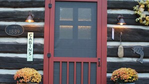 Una baita in legno con una porta rossa, due fioriere di legno con fiori e un cartello che indica 'Cabins for Rent'.
