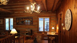 Un accogliente interno di una baita con pareti in legno, un lampadario, un'area pranzo con tavolo e sedie e una sveglia appesa al muro.