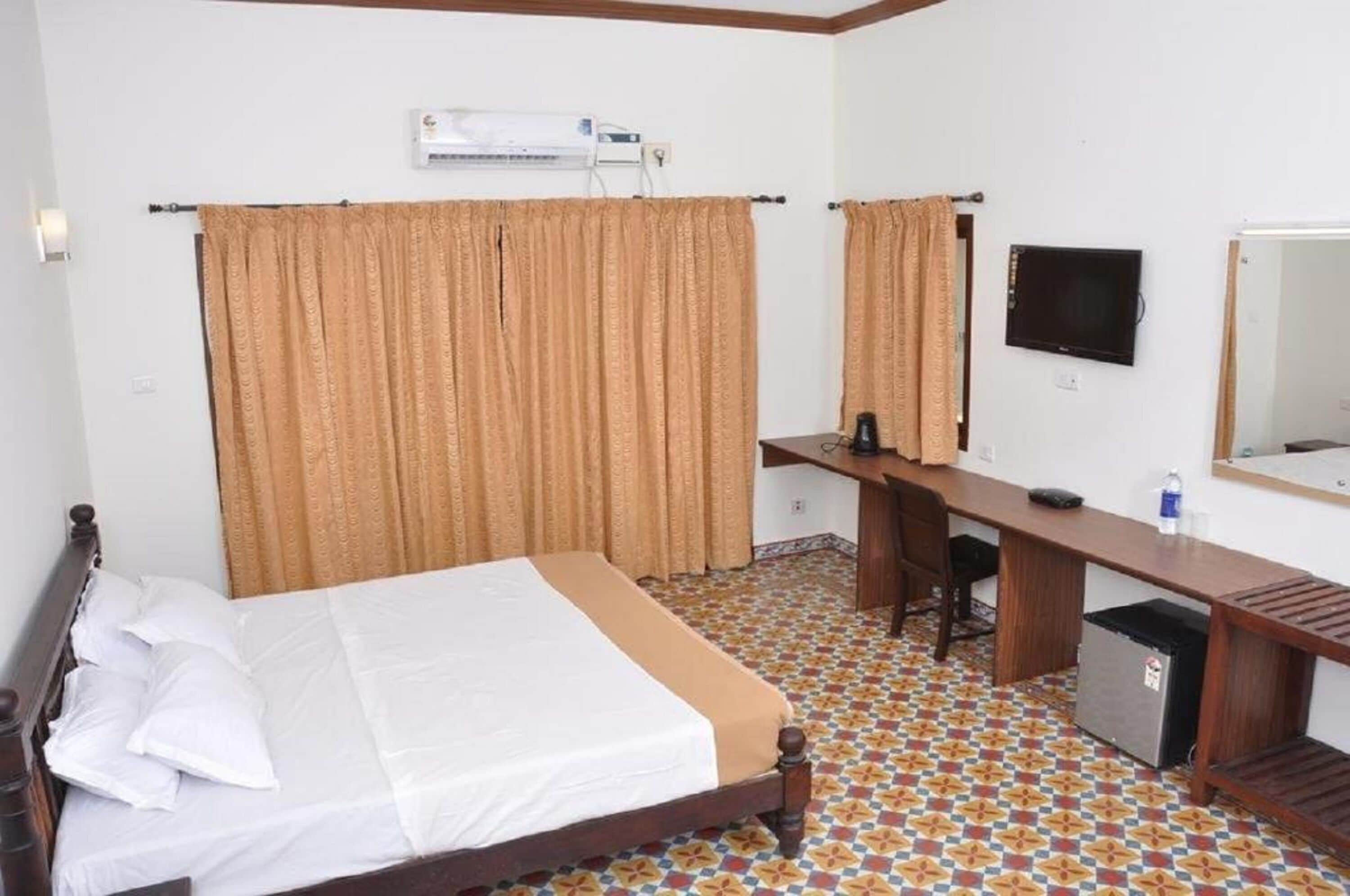 A hotel room with a bed, a desk, a chair, a television, and a refrigerator.