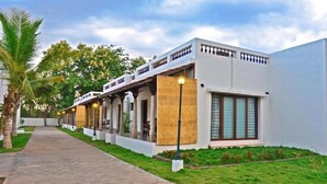 A modern building with a covered walkway, columns, and a well-maintained lawn. - Thappa Gardens Resort (Karaikudi)