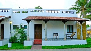 A two-story white building with a tiled roof, a covered porch with a bench, and a small garden area. - Thappa Gardens Resort (Karaikudi)