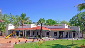 A building with a red-tiled roof, multiple windows, and a covered outdoor area with a playground. - Thappa Gardens Resort (Karaikudi)