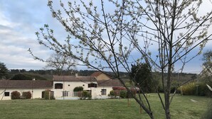 Ein Haus mit einem Ziegeldach, einem eingezäunten Hof und einem Baum im Vordergrund.