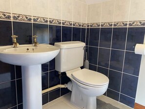 Un baño con un lavamanos blanco, dos grifos dorados, un inodoro blanco y paredes cubiertas de azulejos azul oscuro.
