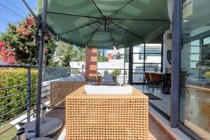 A balcony with wicker furniture, a green umbrella, and a glass door leading to an indoor area with a table and chairs. - Villa in Puerto Marina with private and heated pool (Benalmádena)