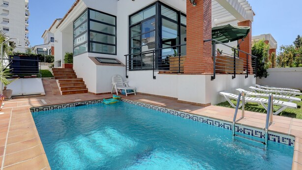 Ein modernes Haus mit Swimmingpool, einer Terrasse mit Liegestühlen und einer Treppe, die zu einem Balkon führt.