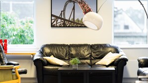 A modern living room with a black leather sofa, a small table with a plant, and a framed picture of a roller coaster on the wall.