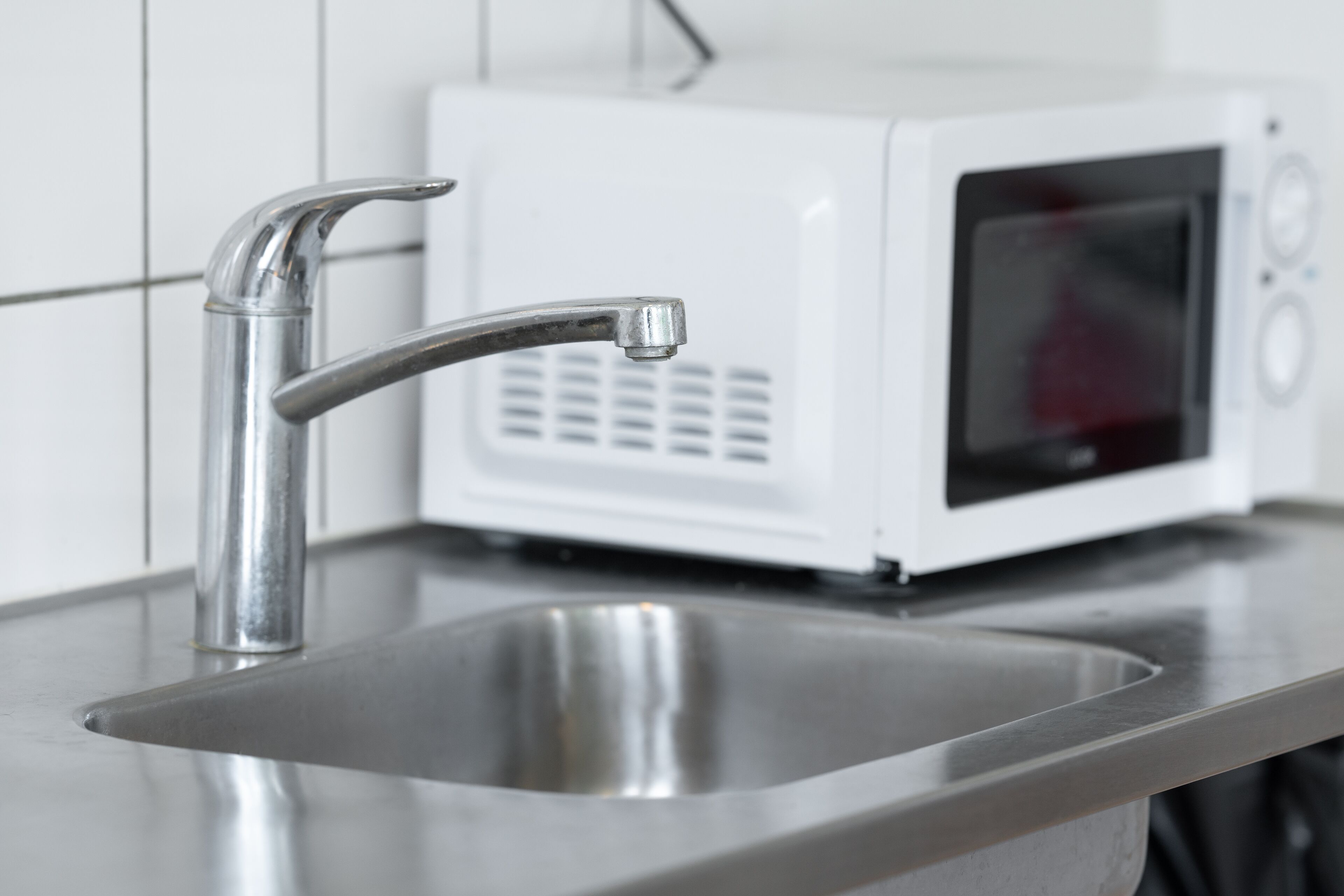A stainless steel kitchen sink with a modern faucet, a white microwave, and a tiled backsplash.