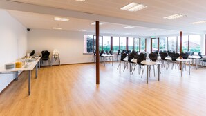 A spacious room with a long table and chairs, large windows, and a wooden floor.