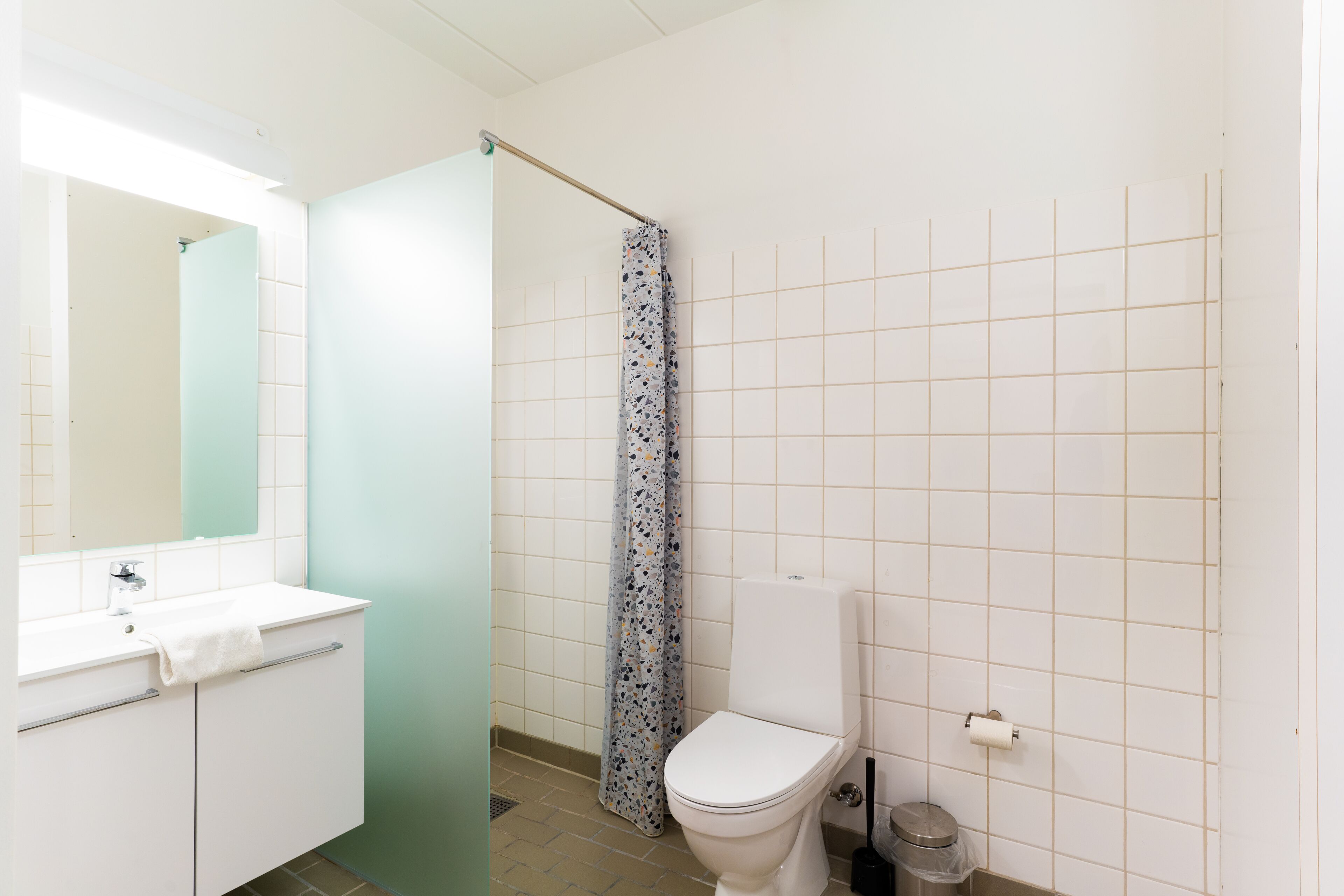 A bathroom with a white sink, mirror, toilet, and shower curtain.