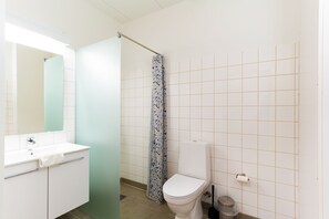 A bathroom with a white sink, mirror, toilet, and shower curtain. - Djurs Housing (Trustrup)