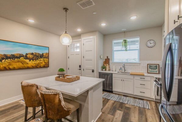 A modern kitchen with white cabinets, a marble island, and a stainless steel refrigerator.