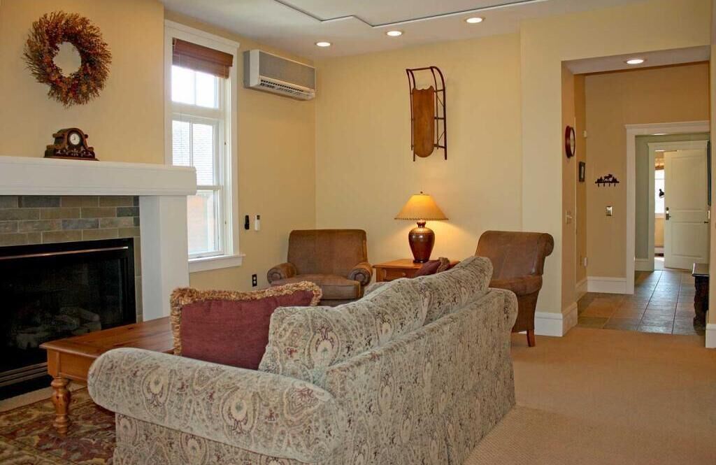 A living room with a fireplace, two armchairs, a sofa, a lamp, and a wall-mounted shelf.