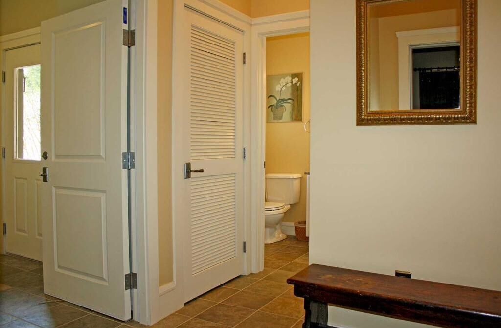 A hallway with closed doors, a toilet visible in the background, and a mirror on the wall.