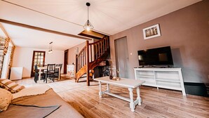 Un salon doté d’un plancher en bois, d’un meuble TV blanc, d’un coin repas avec une table et des chaises, et d’un escalier.