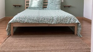 Une chambre à coucher avec un lit, un luminaire en fibres tressées, un mur vert et un plancher en bois.