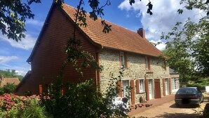 Une maison en pierre avec un toit recouvert de tuiles rouges, une partie en briques et une allée où est garée une voiture.