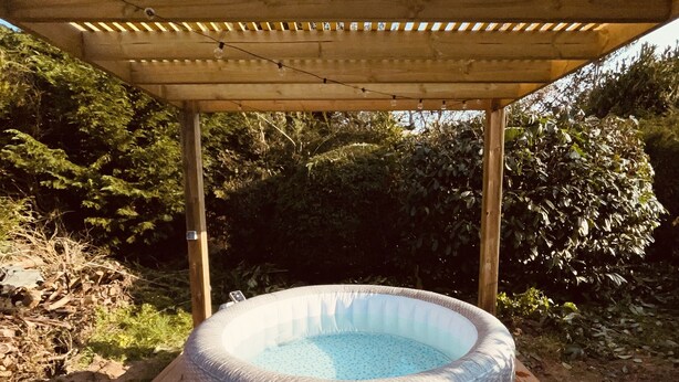 Un bain à remous extérieur, installé sous une pergola en bois, sur une terrasse en bois.