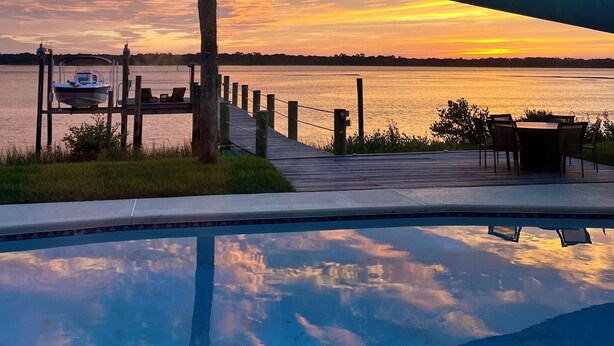 Une terrasse au bord de l’eau avec une piscine, un bateau et un palmier.