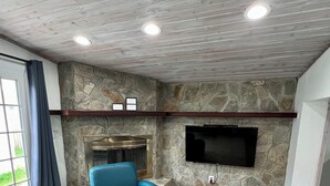 Un salon avec un mur en pierre, une cheminée, un téléviseur à écran plat et un fauteuil en cuir bleu.