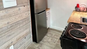 Une cuisine de taille réduite, dotée d’un réfrigérateur en acier inoxydable, d’une cuisinière et de panneaux en bois aux murs.