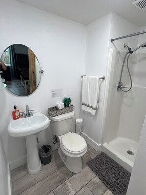 Ein Badezimmer mit Waschbecken, Toilette und Dusche. Über dem Waschbecken hängt ein Spiegel, an der Wand ist ein Handtuchhalter.
