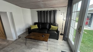 Un salon avec un canapé en cuir noir, deux coussins verts, une table basse en bois et un lampadaire.