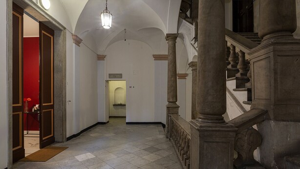 Un couloir doté d’un sol carrelé, d’une porte rouge et d’un escalier orné de colonnes décoratives.