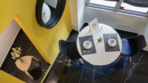 Un coin repas avec une table ronde, deux chaises, un vase de fleurs, un miroir et une fenêtre avec des rideaux.