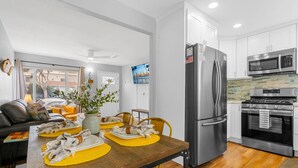 A modern kitchen with stainless steel appliances, a dining area with yellow chairs, and a living room with a sofa and a plant. - Beach-2-Bay 1br | Mission Beach | AC | Shops (San Diego)
