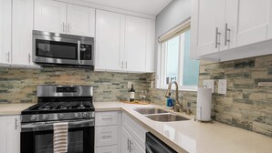 A modern kitchen with white cabinets, a stainless steel microwave, a gas stove, and a dishwasher. - Beach-2-Bay 1br | Mission Beach | AC | Shops (San Diego)