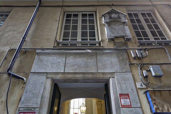 Fachada de edificio con entrada de piedra, una placa y una ventana de diseño calado.
