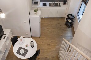 Una cocina moderna con armarios blancos, un microondas y un lavabo. Hay una zona de comedor con una mesa, sillas y una pequeña planta.