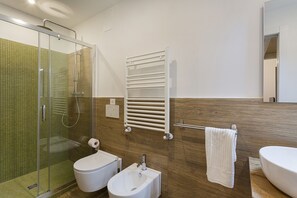 Un baño moderno con cabina de ducha de vidrio, inodoro, bidé, lavamanos, toallero y espejo.