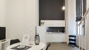 Ett kompakt kök med vita skåp, en svart bänkskiva och en hängande lampa.